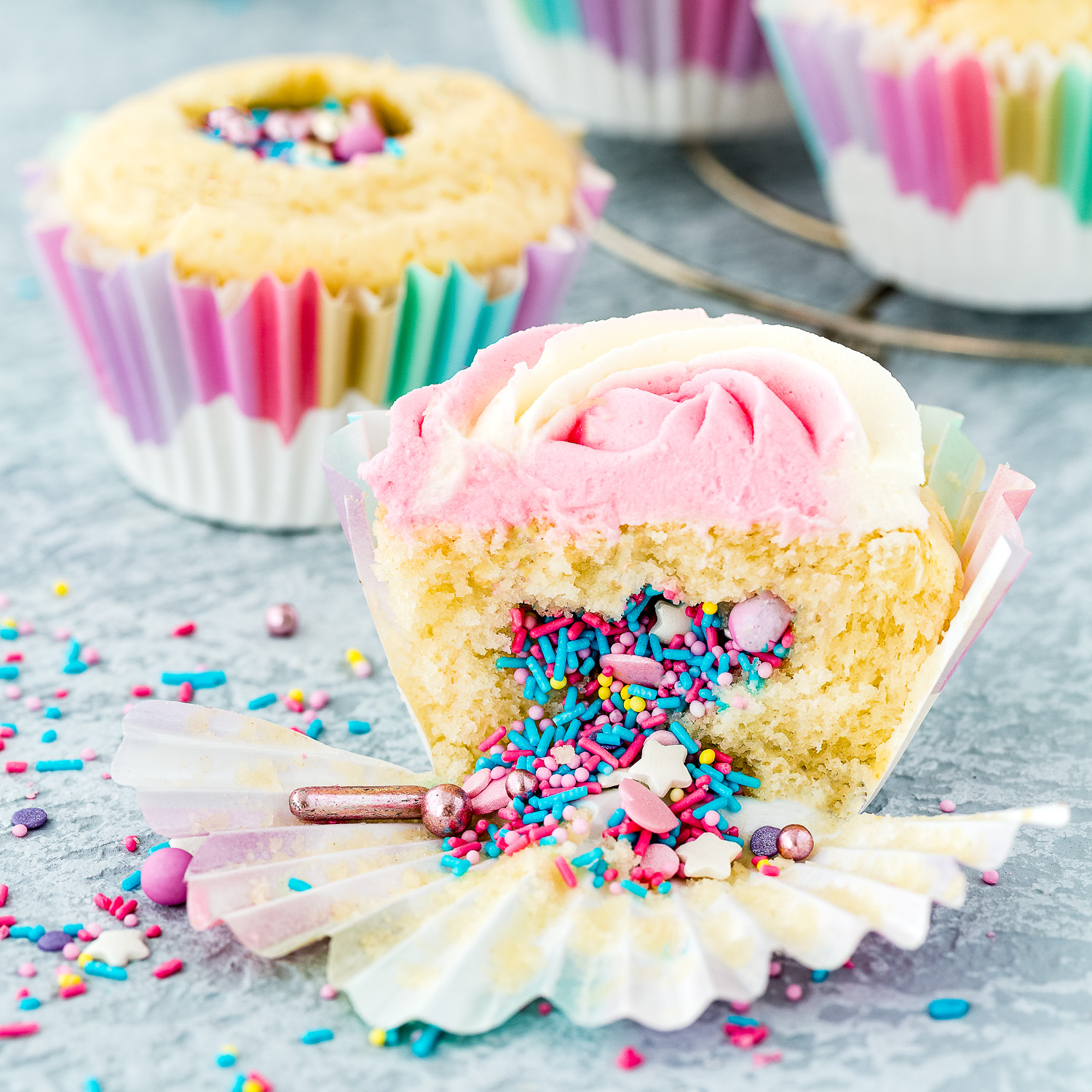 Eggless Sprinkle Surprise Cupcakes over a blue surface.