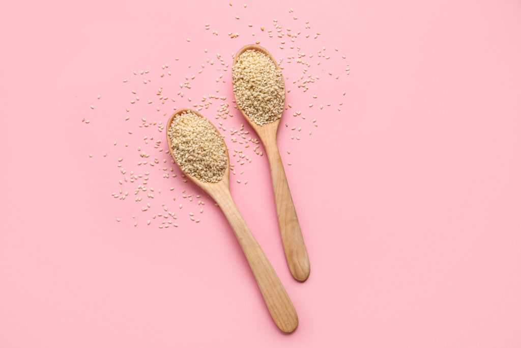sesame seed in two spoons over a pink background,