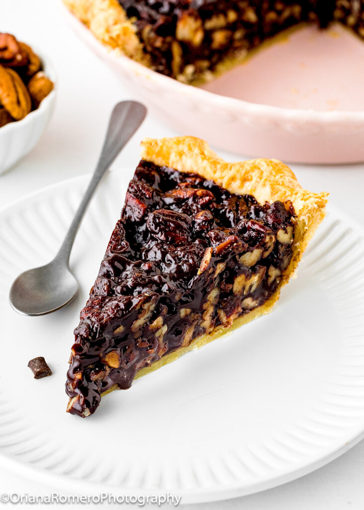 a slice of Eggless Chocolate Pecan Pie on a white plate with a spoon.