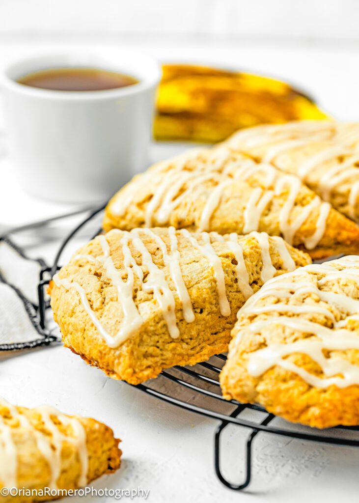 Eggless Banana Scones with maple glaze over a cooling rack with a cup of tea and a banana in the background.